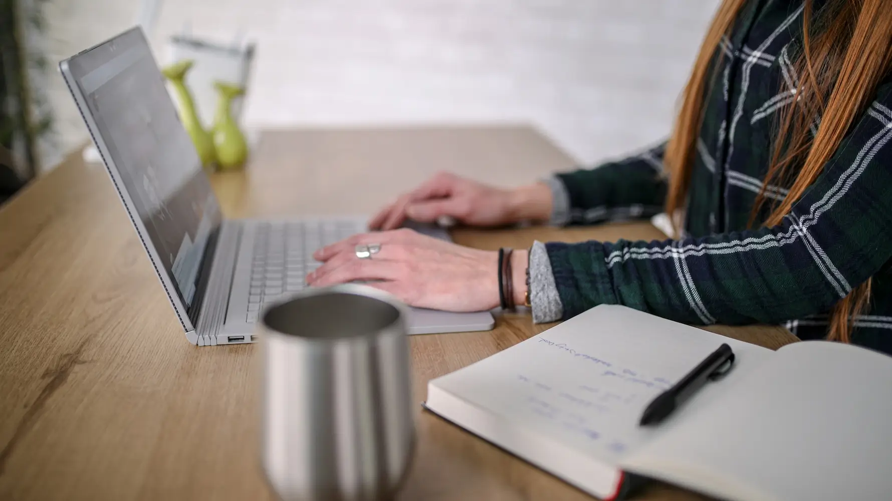 Vrouw werkt op laptop met notitieboek en koffiebeker op tafel
